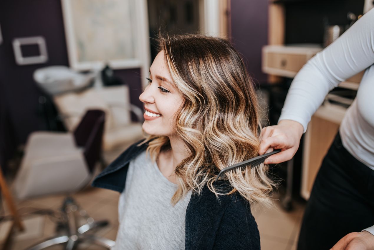 Eine zufriedene Kundin während eines Hairstylings im Friseursalon; im Hintergrund Möbel und ein Friseurwagen für die Organisation.