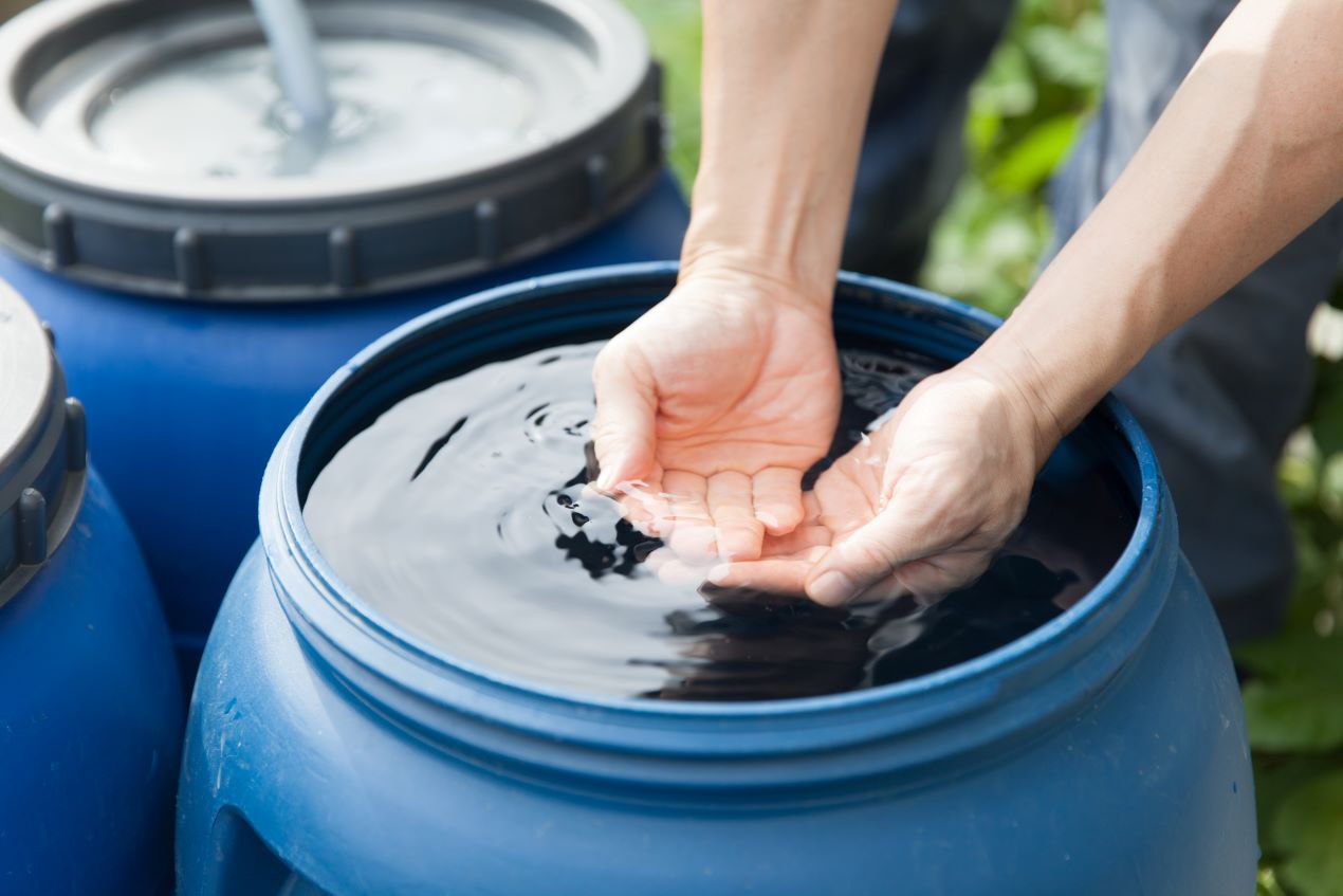 Hände schöpfen Wasser aus einer blauen Zisterne – umweltfreundliche Regenwassernutzung für Haus und Garten